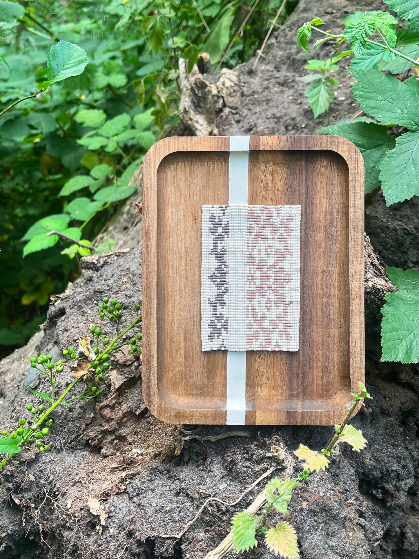 Handwoven floral beaded panel in wood frame set among green foliage outdoors
