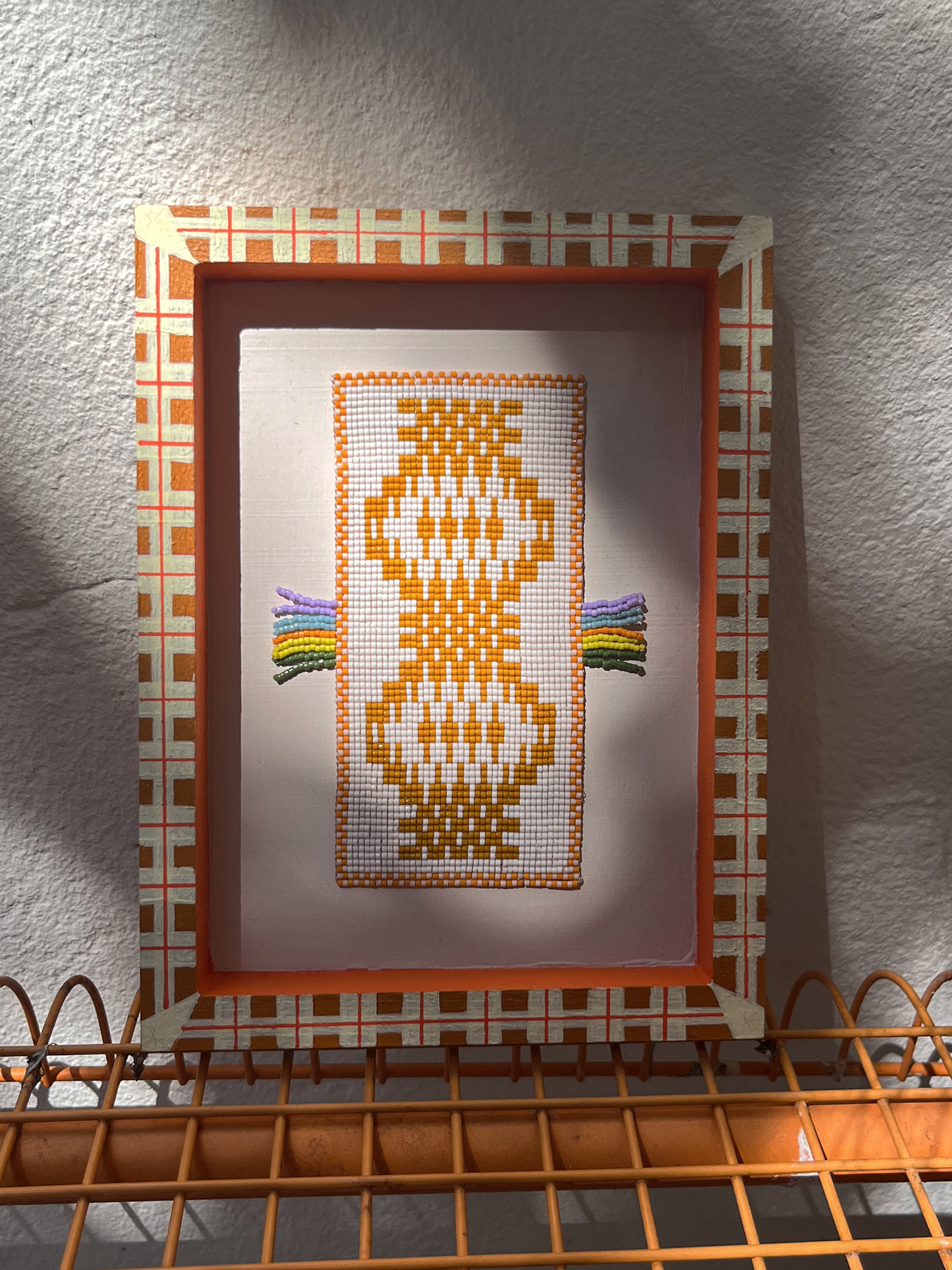 Handwoven beaded panel with colourful fringe arms, photographed in dappled forest light and shadow