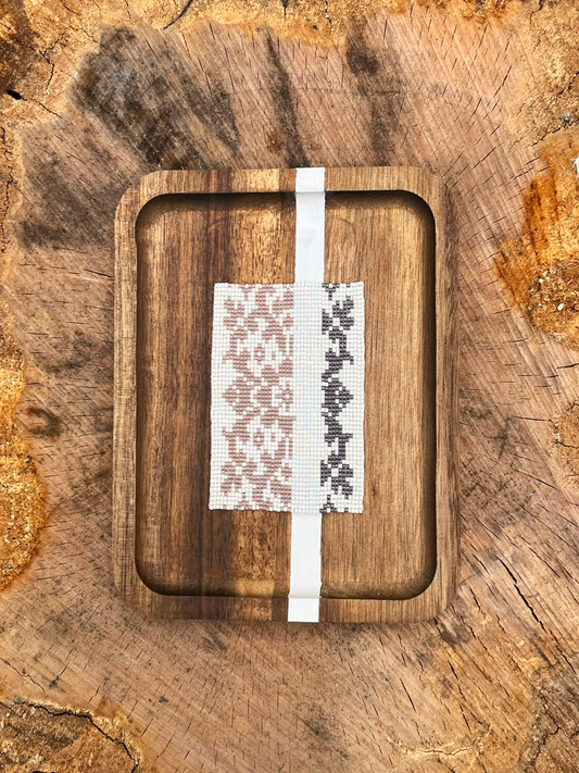 Blush & Coal beaded panel with taupe and charcoal floral pattern on a wood tray, resting on a tree stump