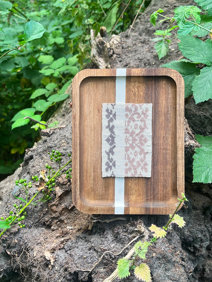 Handwoven floral beaded panel in wood frame set among green foliage outdoors