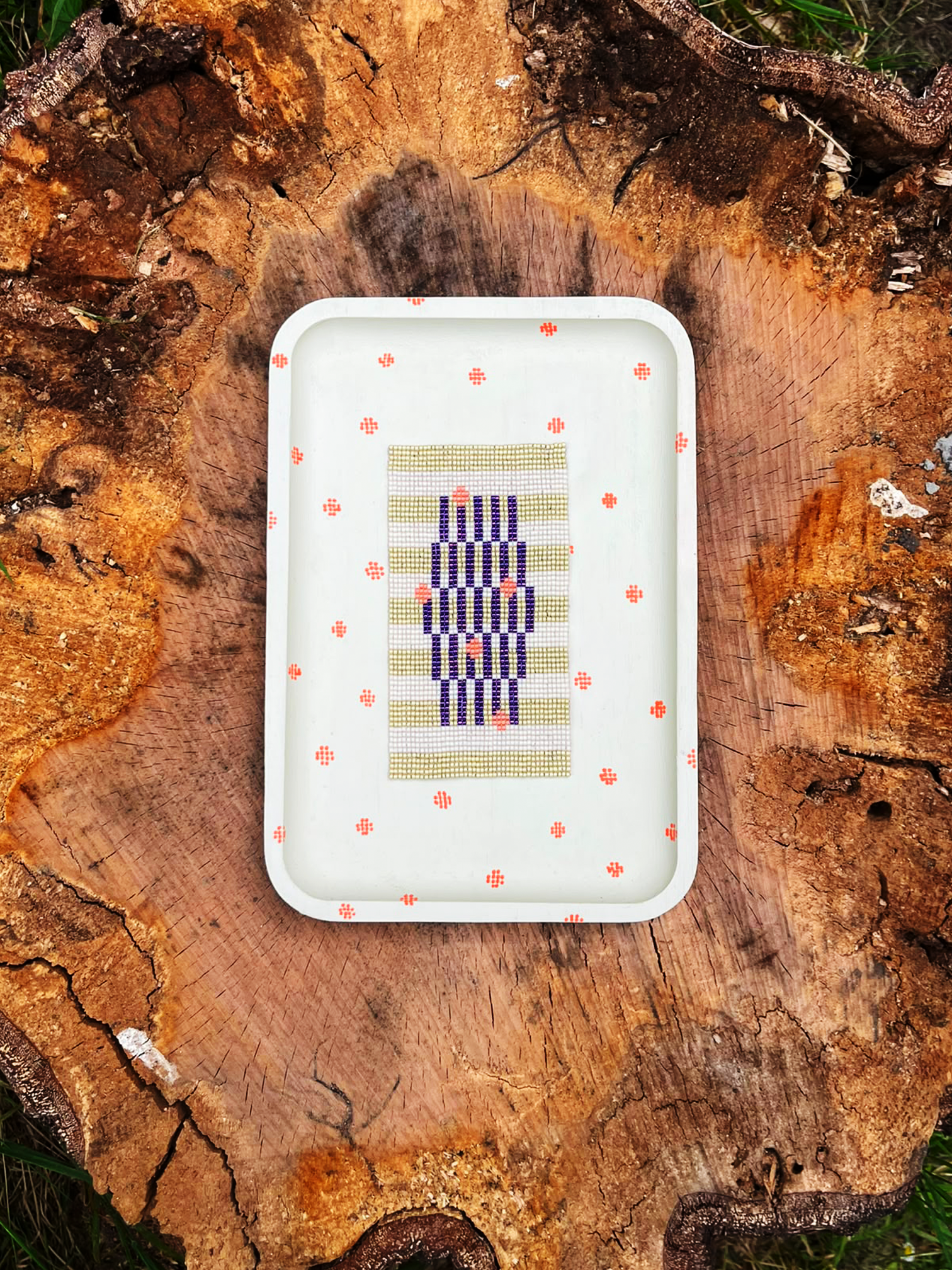 Handwoven beaded panel with sage green and indigo stripes in a cream wood frame with hand-painted coral dots