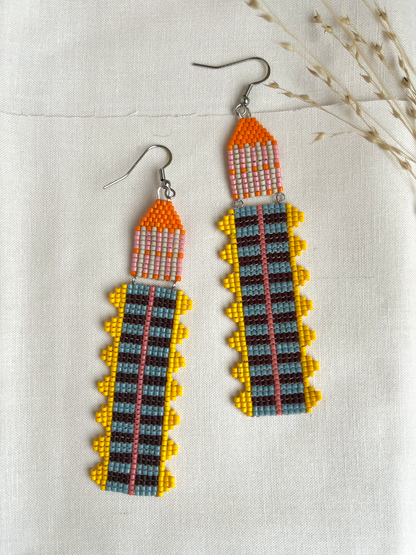 Marigold Temple beaded earrings with orange, yellow, and blue striped fringe on linen fabric
