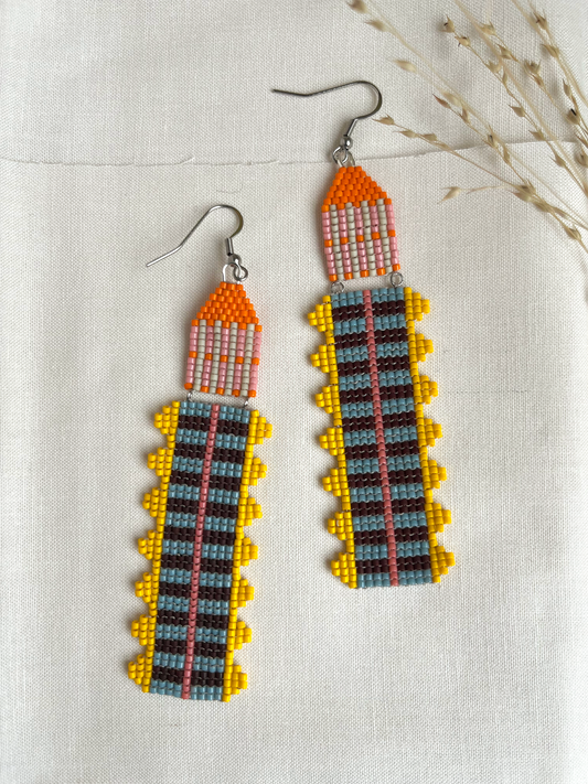 Marigold Temple beaded earrings with orange, yellow, and blue striped fringe on linen fabric