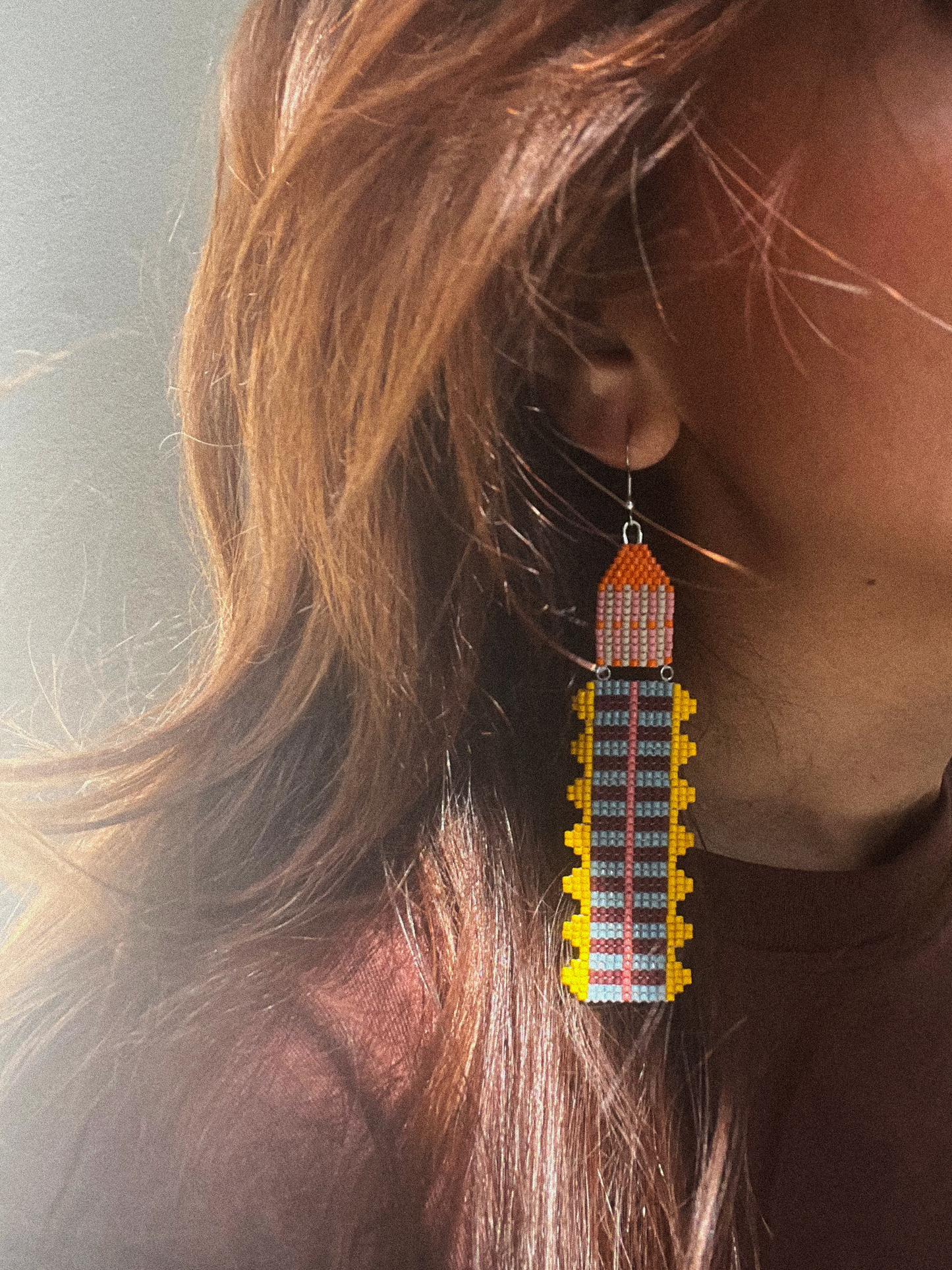 Woman wearing long striped beaded dangle earring, close-up side profile