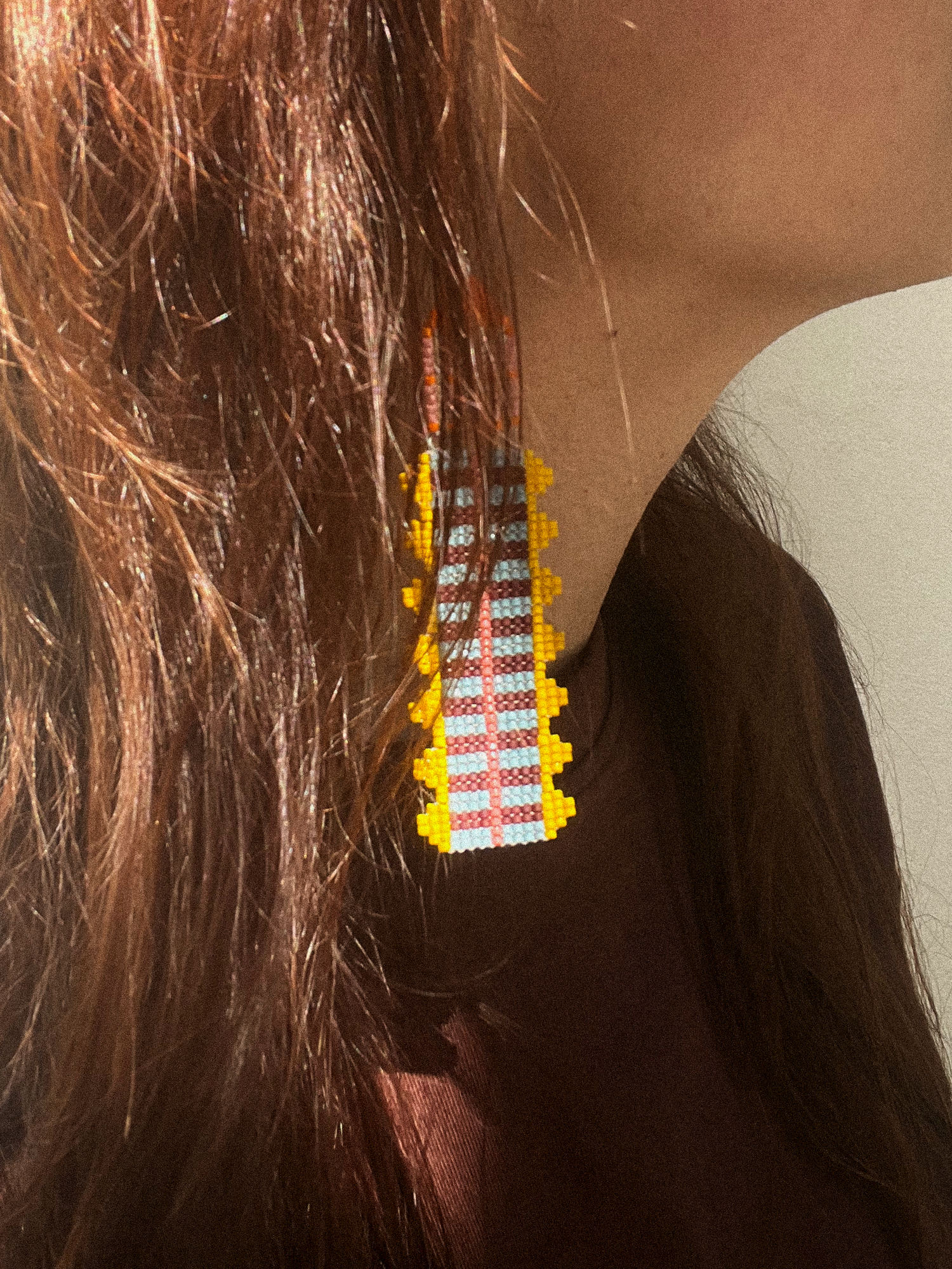 Close-up of handwoven beaded earring with yellow zigzag edge worn against dark hair