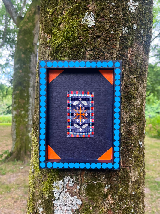 Midnight Bloom beaded panel with navy floral medallion in a blue dotted wood frame, mounted on tree bark
