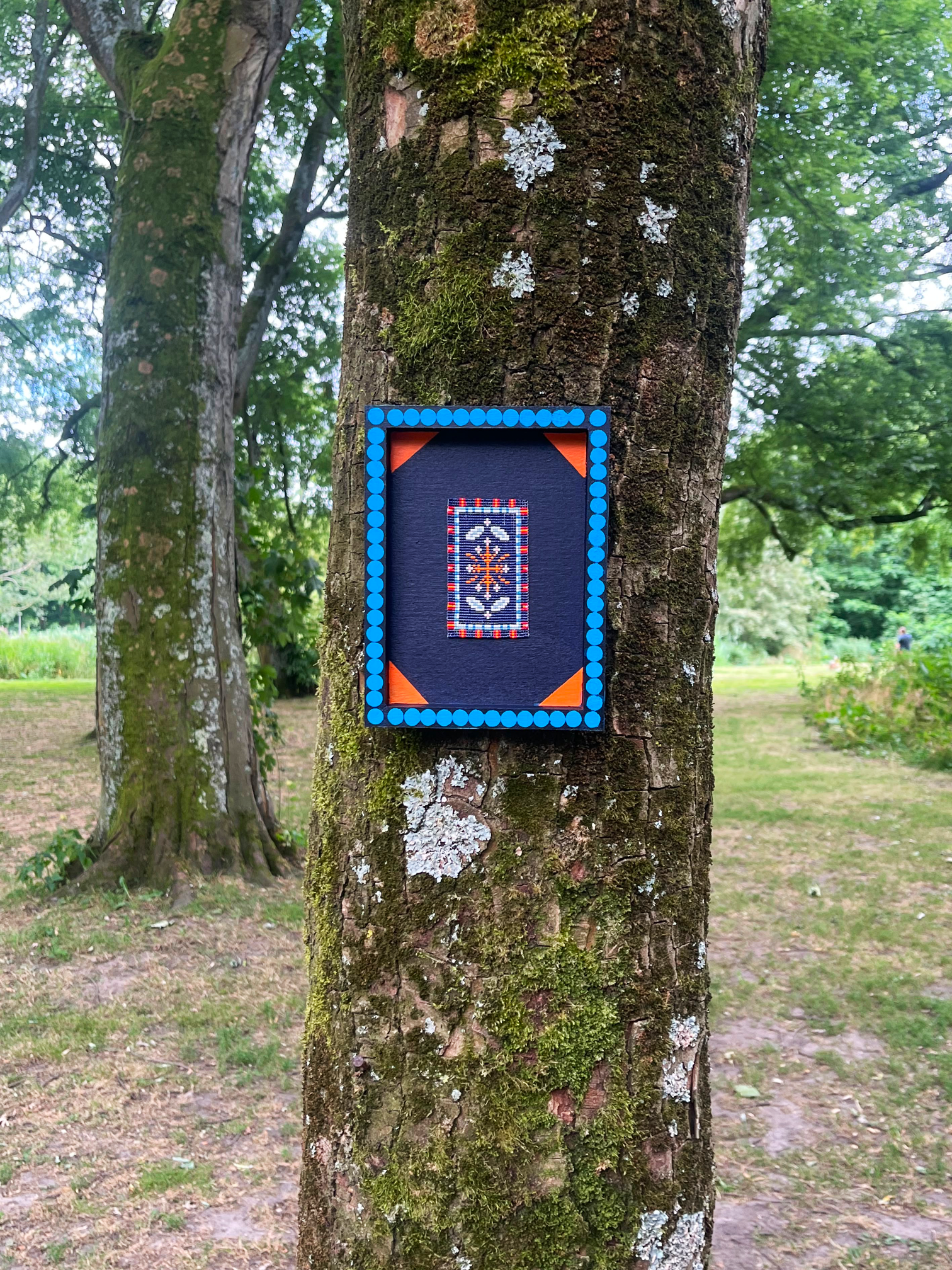 Handwoven navy beaded wall art hanging on a tree trunk in an open field