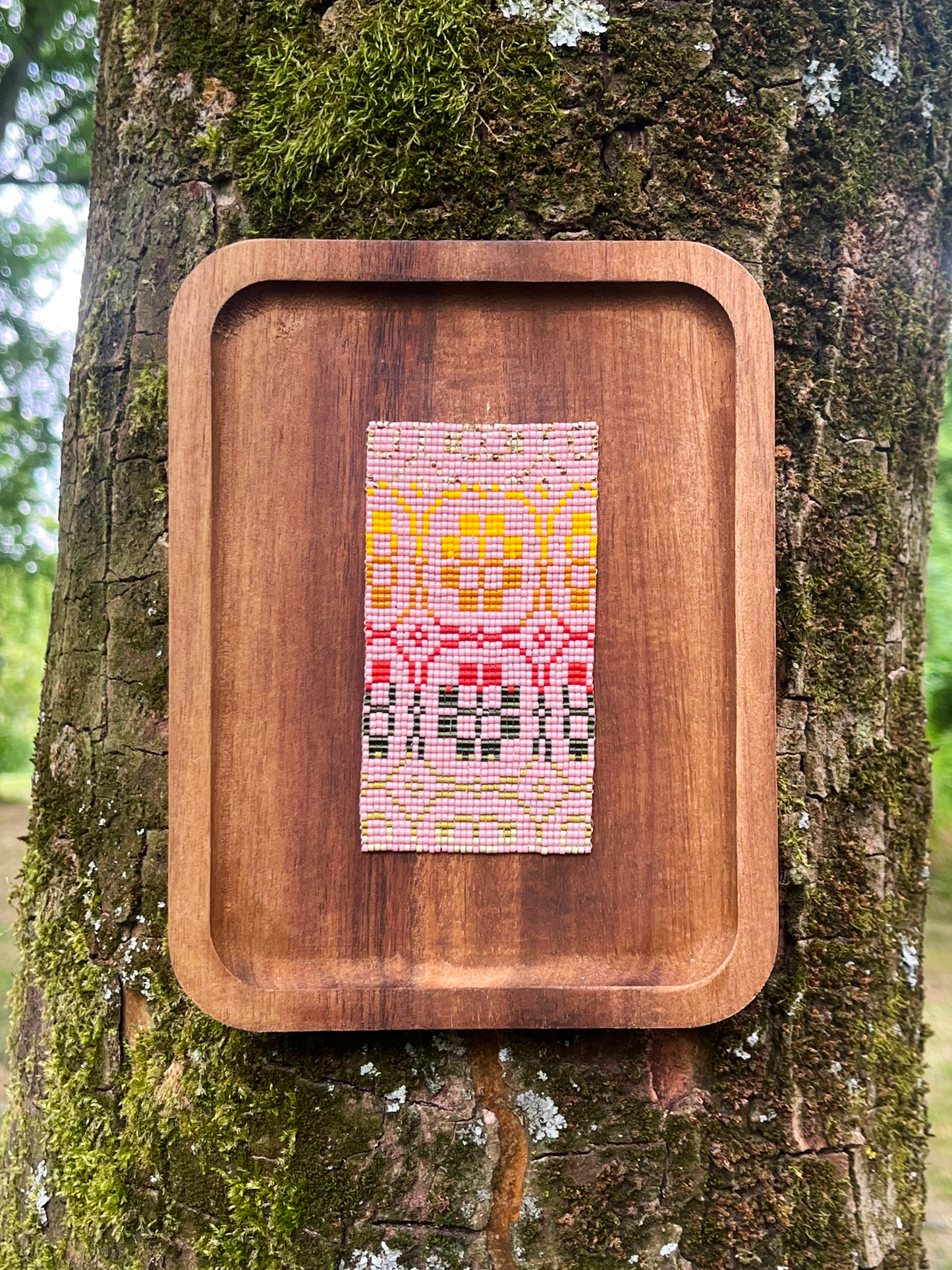 Rose in Bloom beaded panel with pink and gold floral motif on a wood tray frame, mounted on moss-covered tree bark
