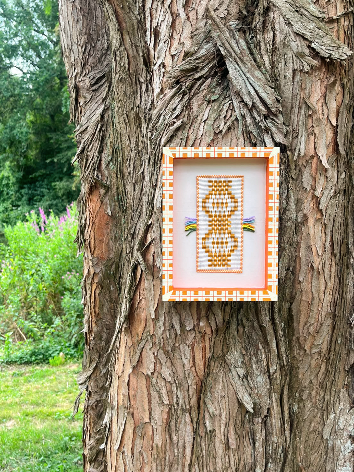 Hand-painted orange and cream plaid frame around a handwoven beaded panel in a forest setting
