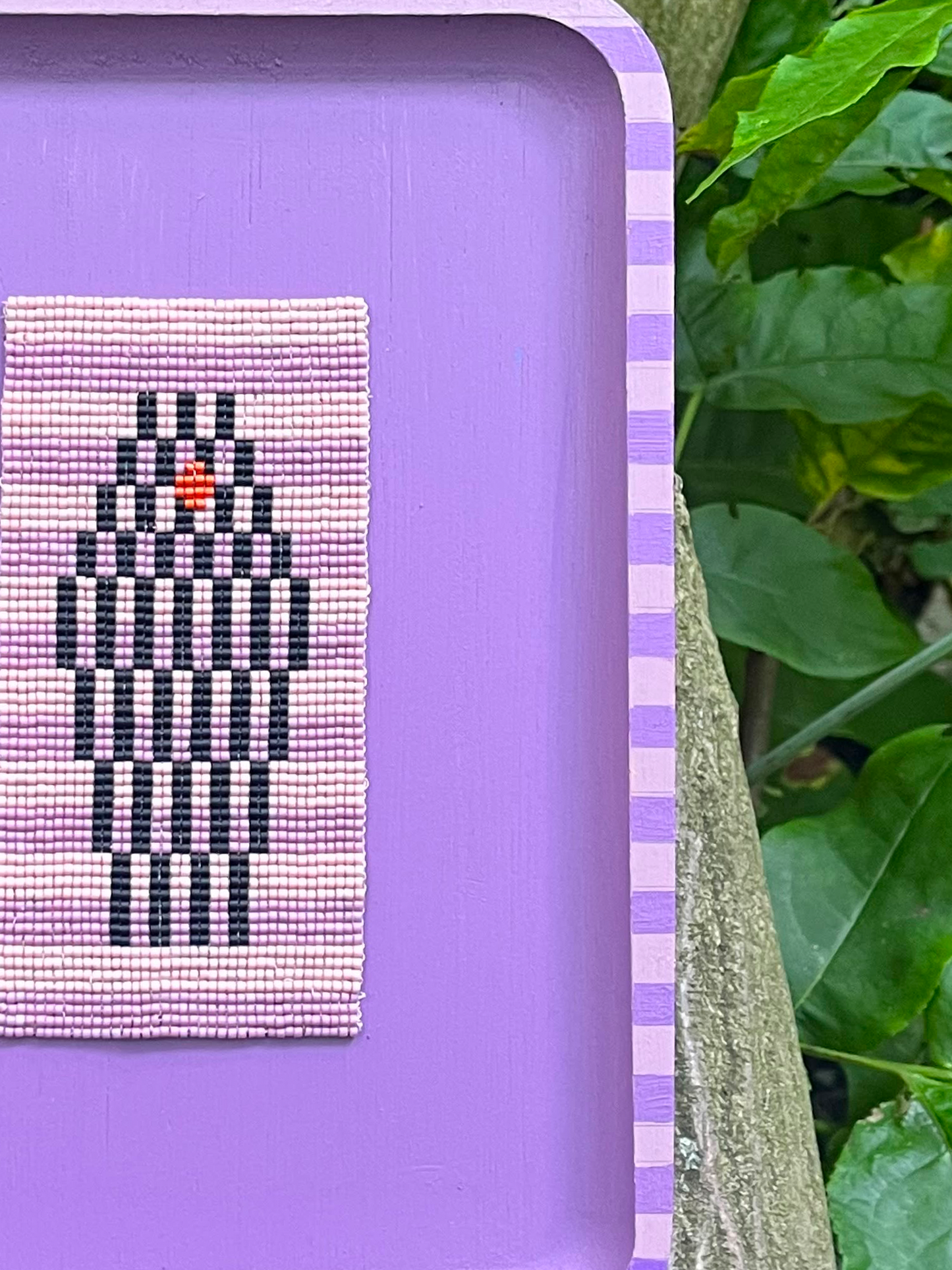 Close-up of lavender striped wood frame around a black and pink geometric beaded panel