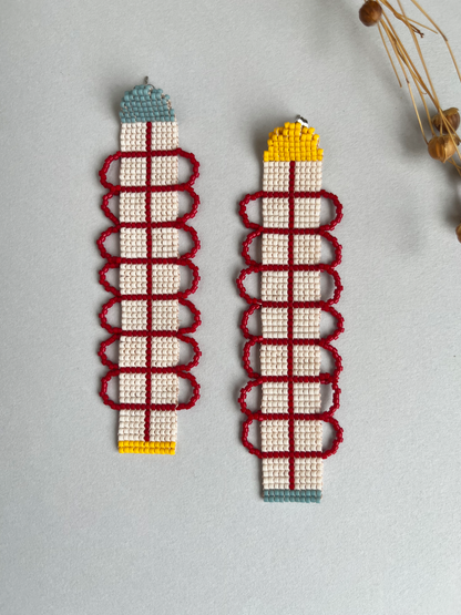 Vine & Spine beaded earrings with red scrollwork pattern, mismatched blue and yellow caps, on grey surface