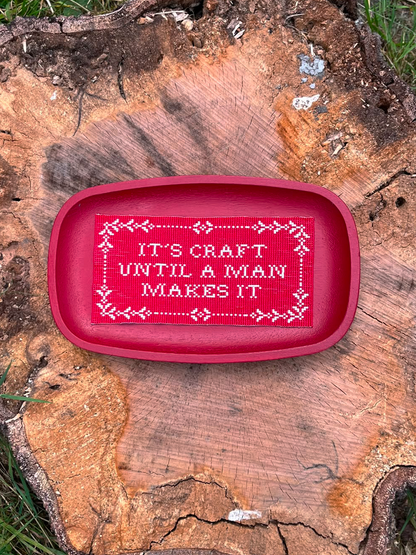 Handwoven red beaded panel with cross-stitch sampler border resting on a tree stump