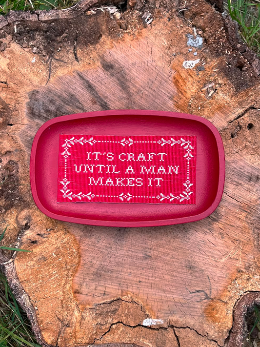 Handwoven red beaded panel with cross-stitch sampler border resting on a tree stump